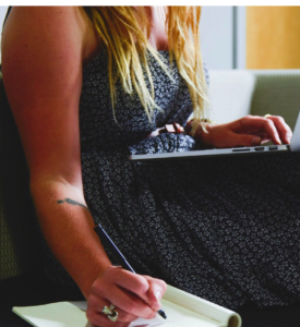 Female working on a computer and making hand notes.